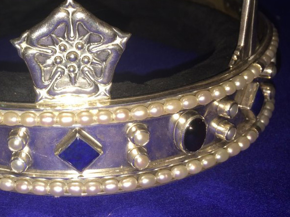Part of a silver crown set with blue stones and pearls, with a silver rose on top