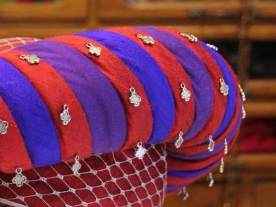 Part of a hat with a padded roll, wrapped in spiral bands of coloured silk, with little silver decorations