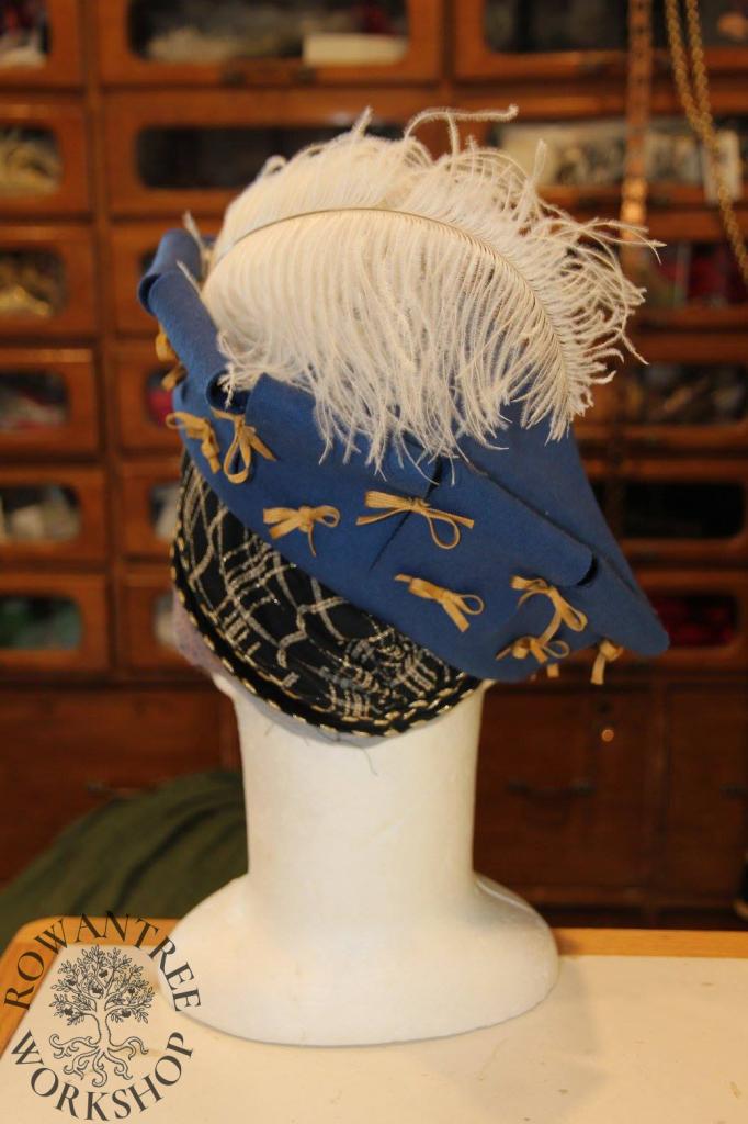 Back view of headform with black hairnet and blue hat with feather