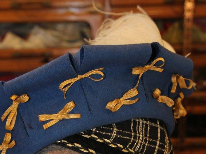 Part of a hat of blue wool with slashed brim held together with bows, over a cap made of gold and black net