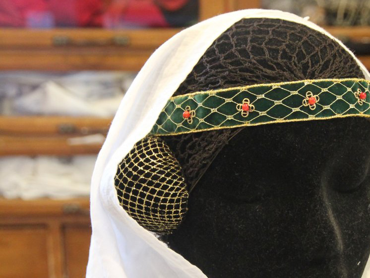 Head mannequin wearing a decorated band around the head, half-round hair covers with gold net, and a veil