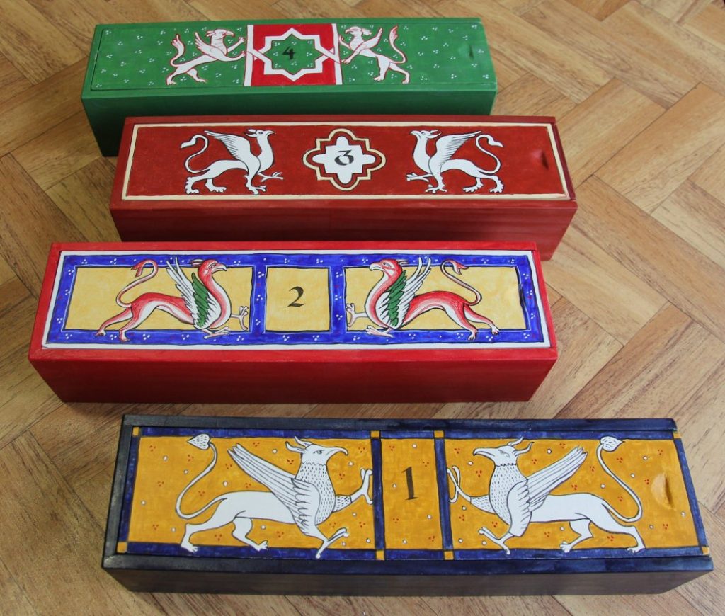 Four rectangular boxes sitting on table, pained in different medieval designs with griffins