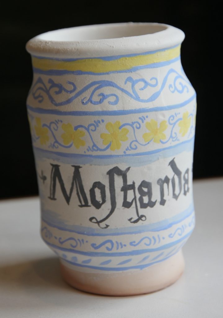 Unfired pot with design and the word 'Mostarda' painted on