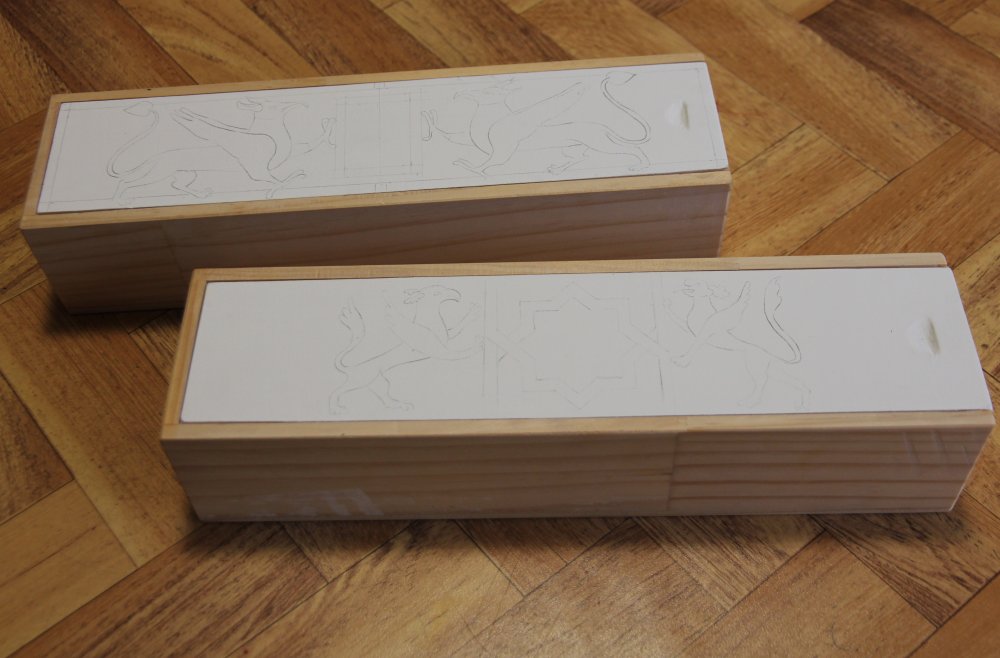 Two wooden boxes with white lids and griffins sketched on the top