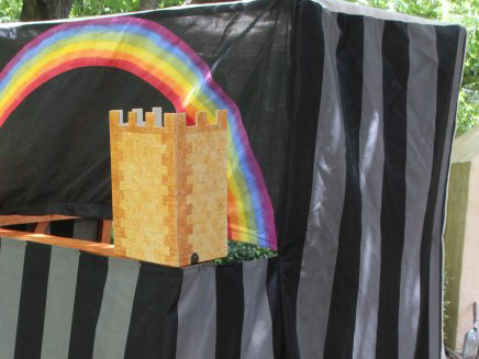 Part of a puppet theatre, with a castle prop and rainbow background