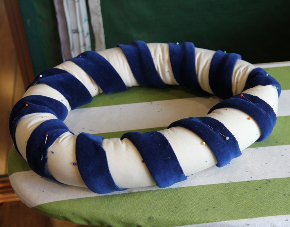 Padded roll lying on bench, with a strip of blue velvet wraped around in a spiral
