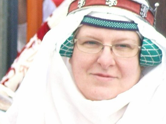 Woman wearing a green fillet and half-round hair covers near the ears, with a white veil and wimple