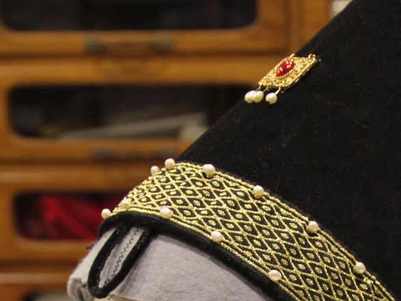 Part of a hat showing gold braid and pearls