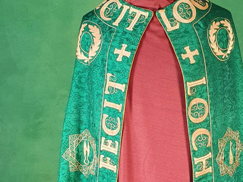 Top of a cloak in green silk with the words Fecit Lochac and wreaths in gold embroidery