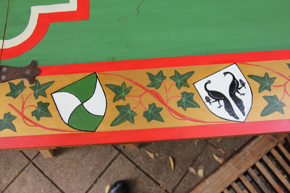 Edge of a table showing painted decoration with ivy leaves and heraldic shields