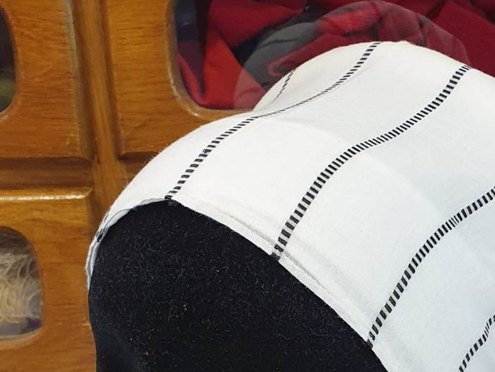 Part of a woman's linen headwear, with black stripes and bulge at the back