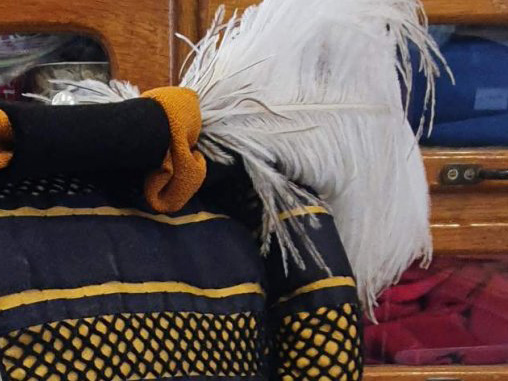 Part of a hat with feather over an undercap with striped decoration