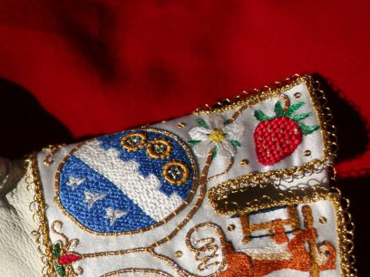 Part of an embroidered glove cuff, with animals, plants and an heraldic shield in silk and gold