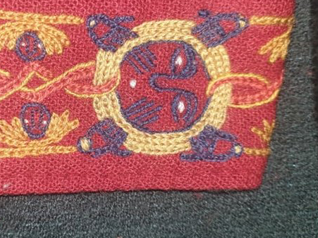 Red wool embroidered in many colours, showing a stylised face