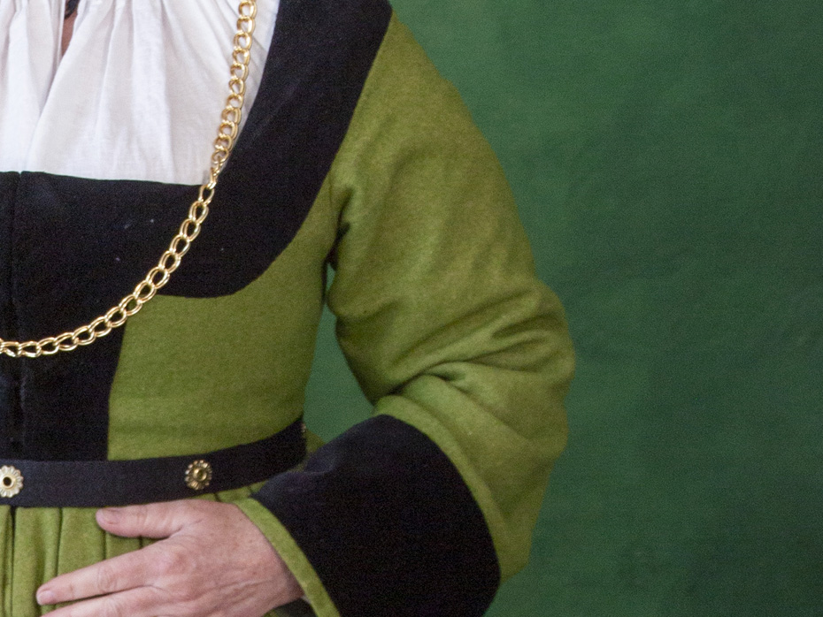 Torso of a woman wearing a German gown in green wool with wide sleeves and deep black velvet trim