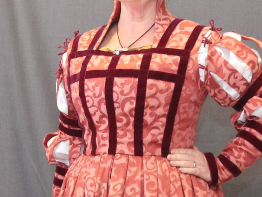 Torso of a woman wearing a German gown with a hugh neck and closed front, decorated with bands of velvet ribbon