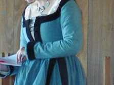 Torso of a woman wearing a German gown in blue linen, with narrow sleeves and black velvet trim