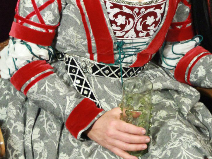 Torso of a woman wearing a German gown in grey brocade with red velvet trim and a pearled breastband