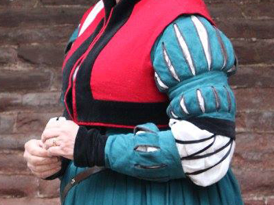 Torso of woman wearing a German gown in teal. The sleeves have 3 rows of large decorative slashes.