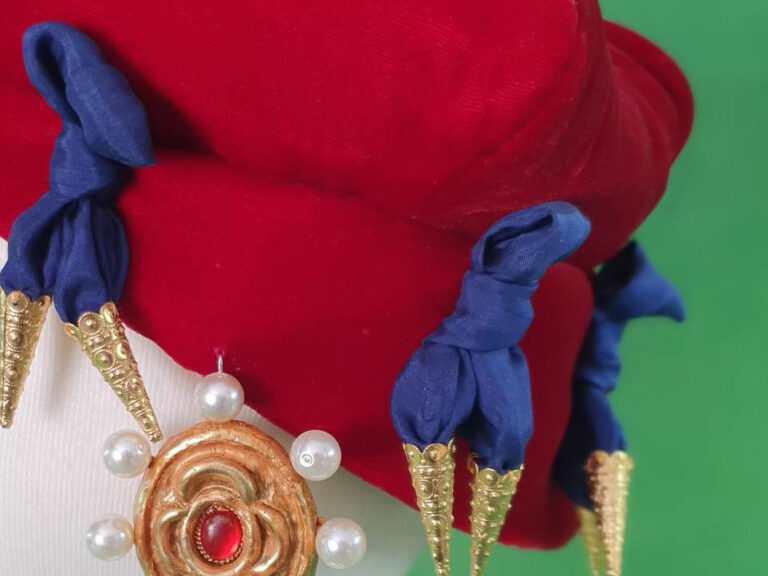 Part of a red velvet hat with blue bows and hanging jewel